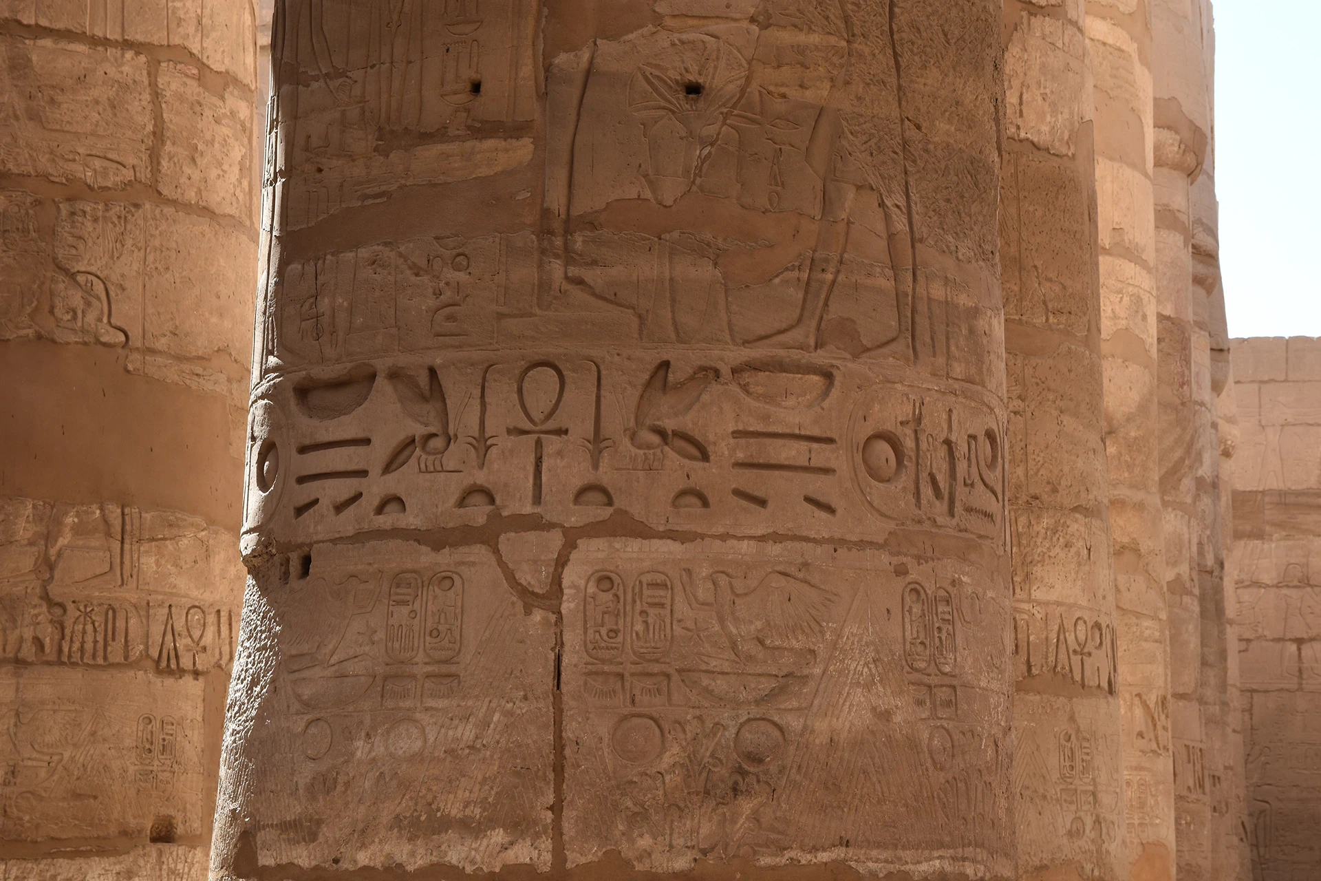 A close-up view of one of Karnak's grand columns reveals intricate hieroglyphs and symbols carved deep into the stone. These ancient inscriptions, bathed in warm sunlight, offer glimpses into the rich religious and historical narratives of pharaonic Egypt.