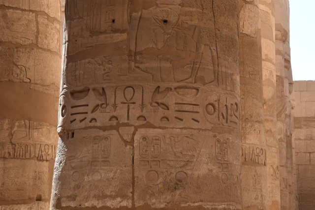 A close-up view of one of Karnak's grand columns reveals intricate hieroglyphs and symbols carved deep into the stone. These ancient inscriptions, bathed in warm sunlight, offer glimpses into the rich religious and historical narratives of pharaonic Egypt.