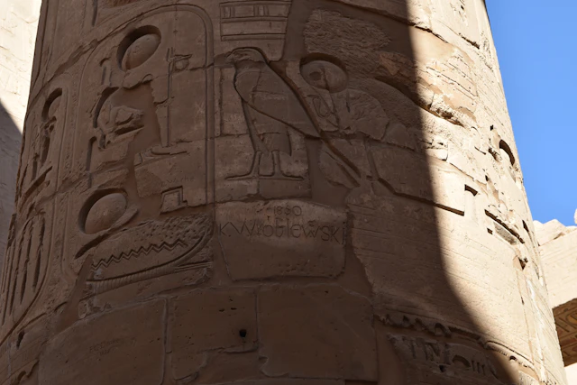 A detailed view of one of the intricately carved columns at Karnak Temple reveals hieroglyphs alongside the engraved name of K. Wroblewski, dated 1850. This 19th-century inscription, while considered a form of damage today, serves as a reminder of historical attitudes toward archaeological sites.