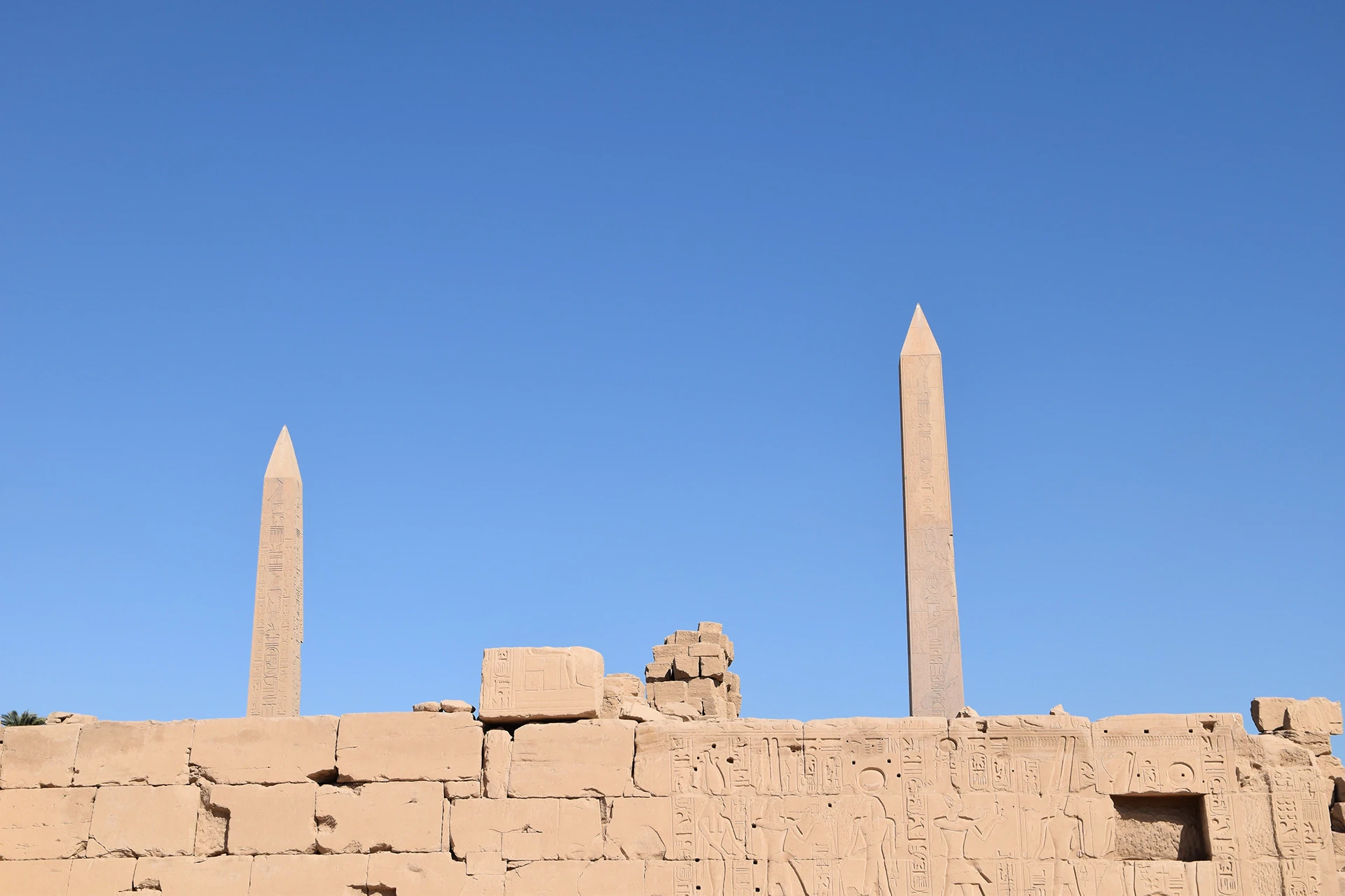 Two towering obelisks pierce the clear blue sky at the Karnak Temple complex, standing as monumental tributes to ancient Egyptian pharaohs. These intricately inscribed pillars symbolize power and divine connection, casting a legacy of awe and reverence across millennia.