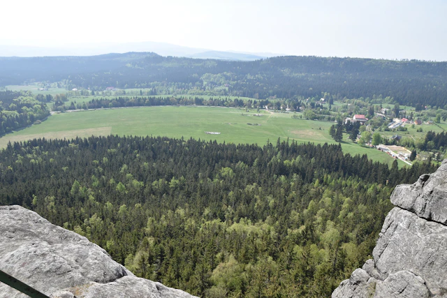 A breathtaking vantage point from the Table Mountains near Kudowa Zdroj showcases a patchwork of dense forests and vast green plains below. The landscape unfolds with scattered rural settlements nestled among the natural beauty.