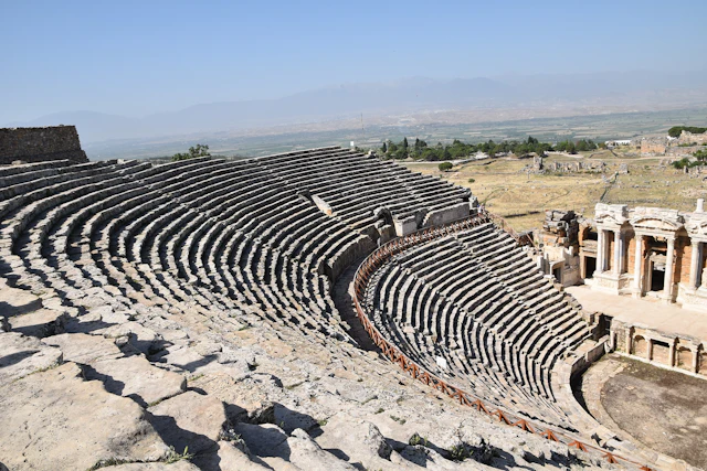 A panoramic view of the ancient theater of Hierapolis, showcasing its well-preserved tiered seating that once hosted thousands, with the vast ruins stretching across the landscape.