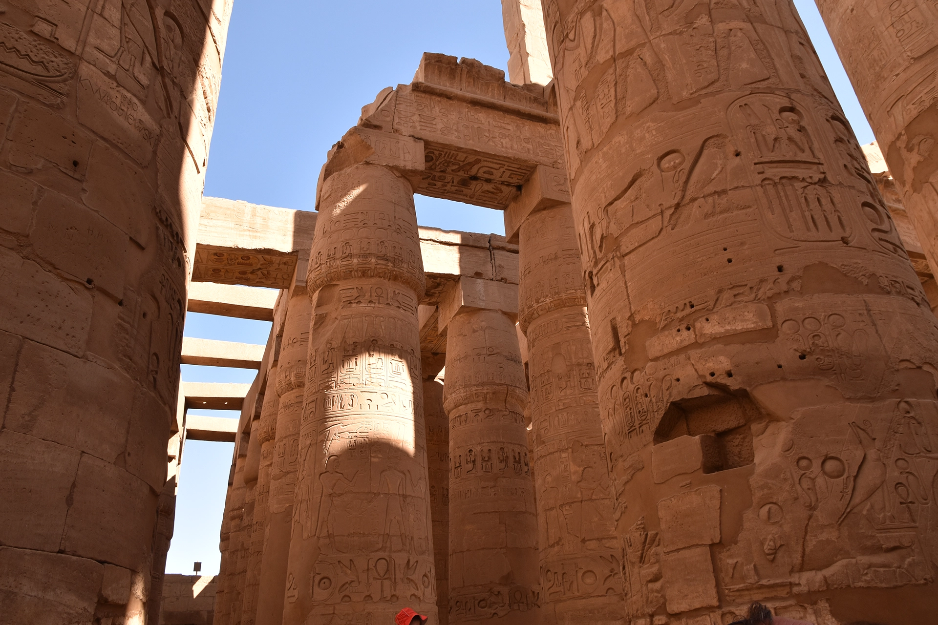 Sunlight cascades onto the colossal inscribed columns of Karnak's hypostyle hall, illuminating the intricate hieroglyphs and ancient carvings. The grandeur of these towering pillars stands as a tribute to the engineering mastery of ancient Egypt.