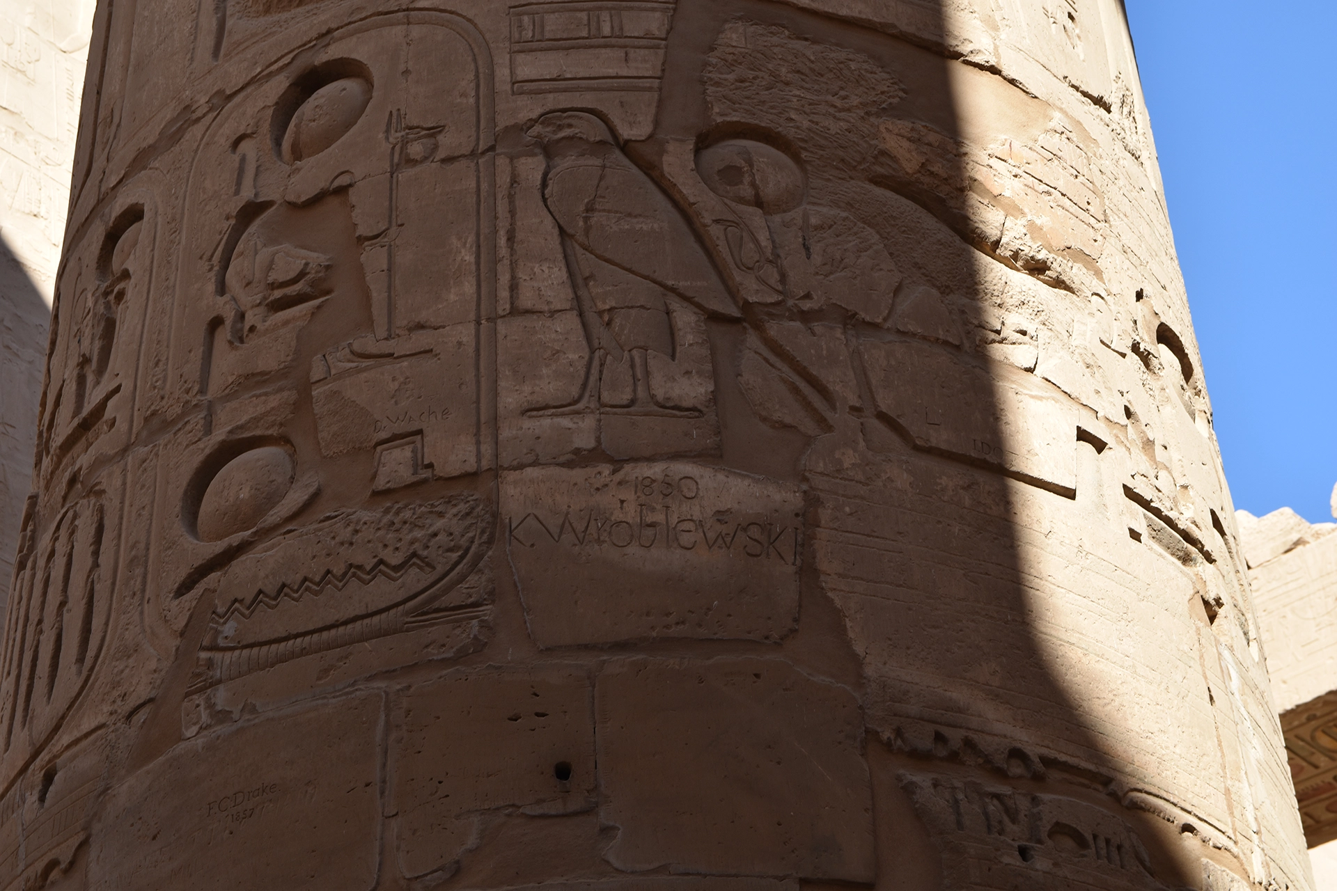 A detailed view of one of the intricately carved columns at Karnak Temple reveals hieroglyphs alongside the engraved name of K. Wroblewski, dated 1850. This 19th-century inscription, while considered a form of damage today, serves as a reminder of historical attitudes toward archaeological sites.