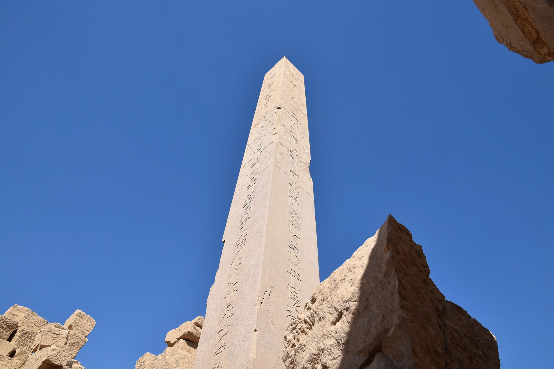 An awe-inspiring view of a towering obelisk at Karnak, its ancient inscriptions etched deep into the polished stone. This monolithic structure, reaching skyward, reflects the architectural mastery and spiritual aspirations of the New Kingdom pharaohs.