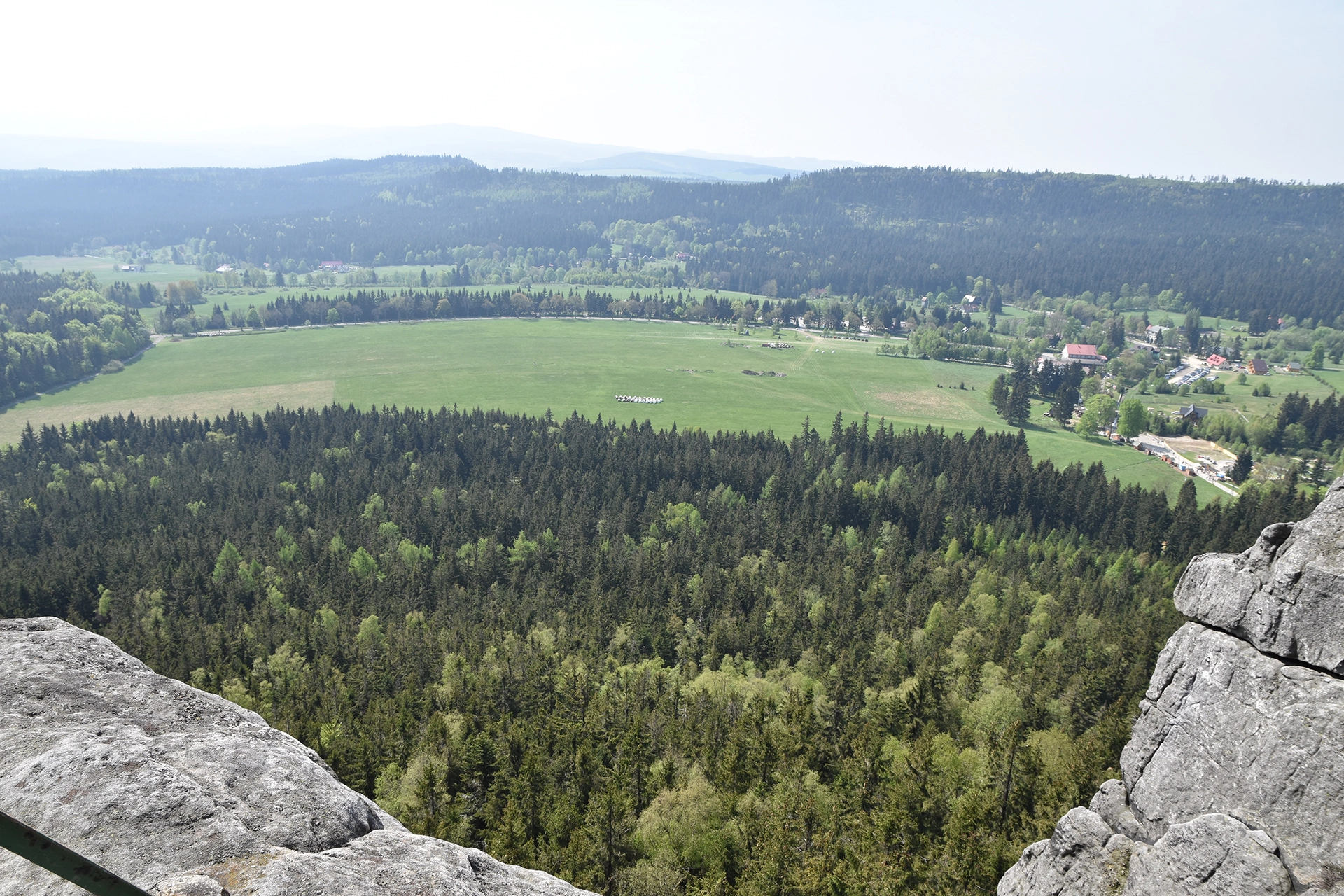 A breathtaking vantage point from the Table Mountains near Kudowa Zdroj showcases a patchwork of dense forests and vast green plains below. The landscape unfolds with scattered rural settlements nestled among the natural beauty.