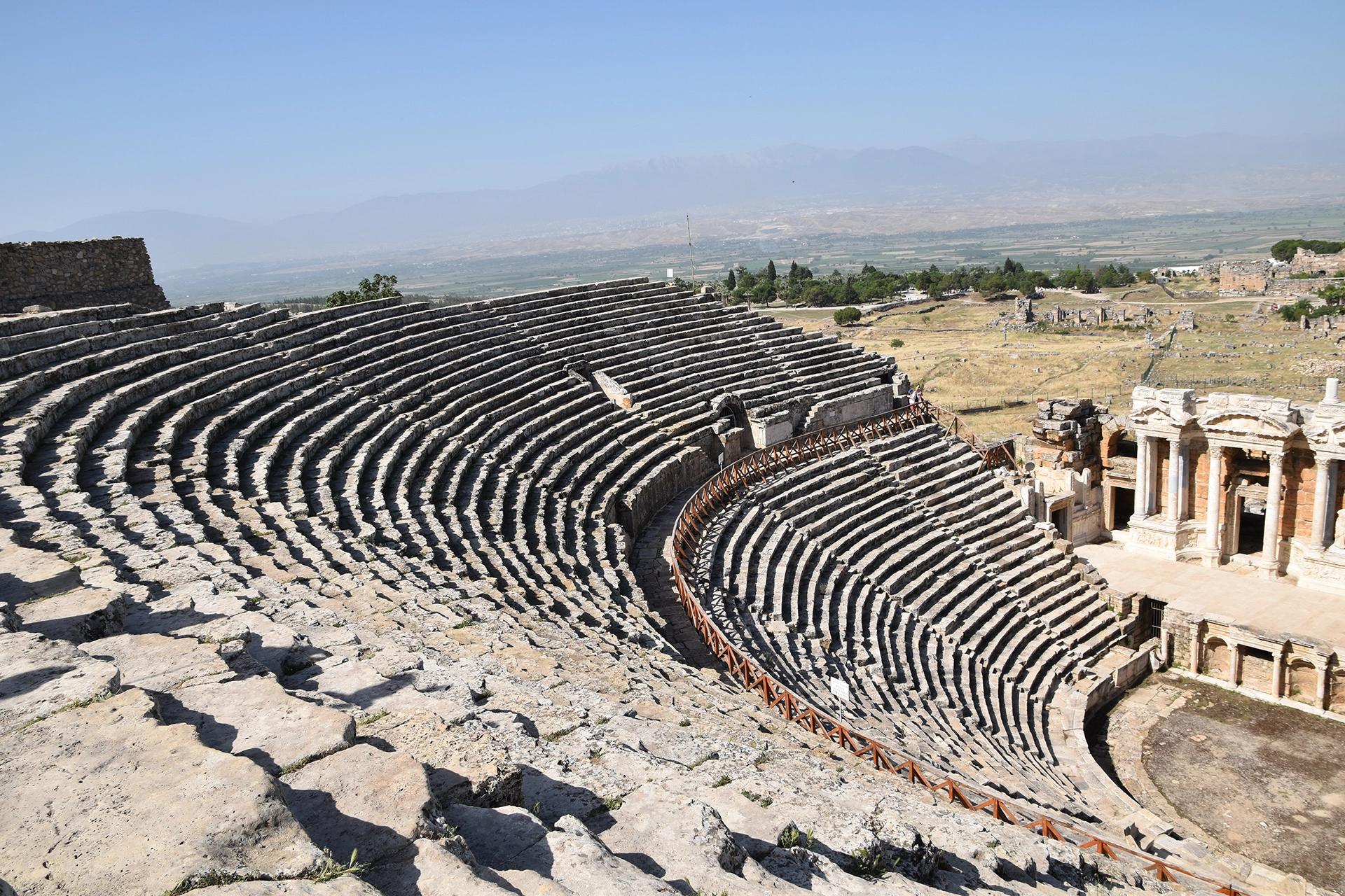 A panoramic view of the ancient theater of Hierapolis, showcasing its well-preserved tiered seating that once hosted thousands, with the vast ruins stretching across the landscape.